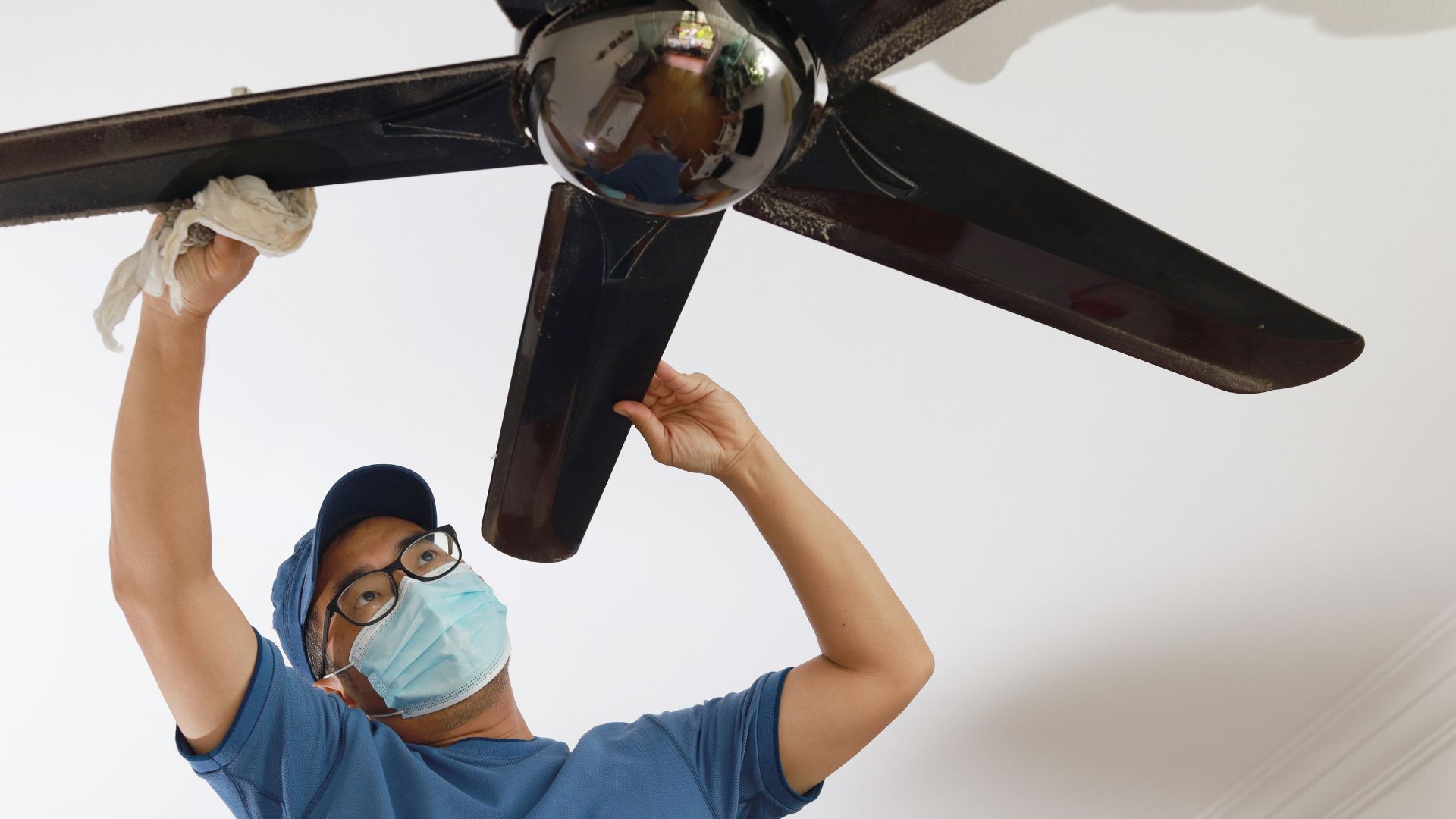 Men cleaner wiping dust from ceiling fan
