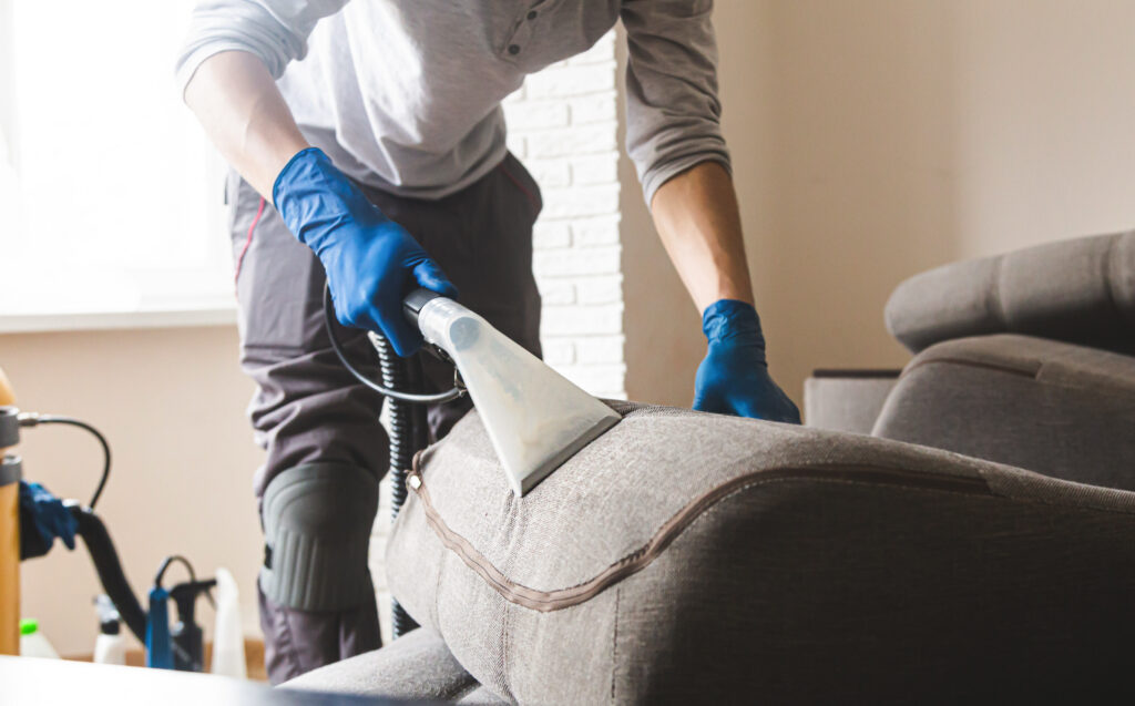 Dry cleaner's man employee removing dirt from furniture in flat, closeup, vacuum clean sofa with professional equipment.
